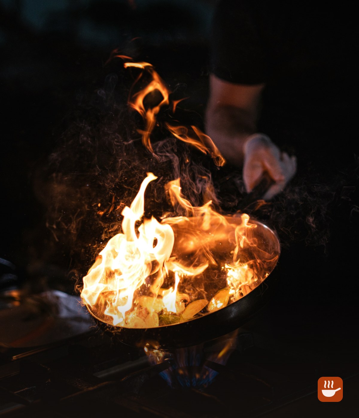 Carbon steel wok over a high flame in a dark kitchen
